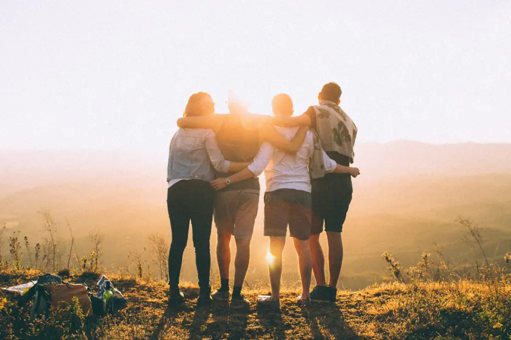 Quatre codeurs embrassés regardant le soleil couchant sur une colline.