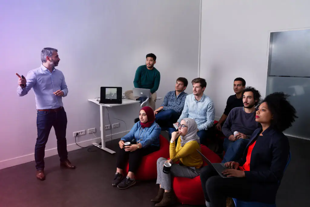 Présentation Inside TCM : équipe diversifiée en réunion, animateur parlant devant un écran.