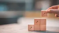 Illustration symbolique de la croissance et du progrès : main empilant des cubes avec des flèches vers le haut